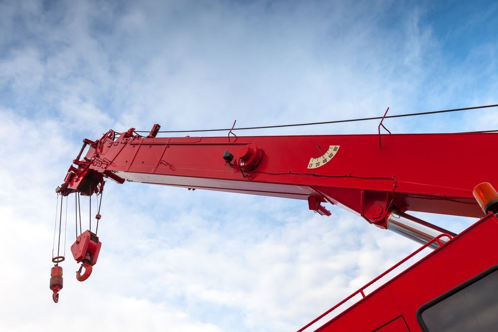 Close-up of a red crane boom with hook and pulley system, showing lifting equipment against the sky.