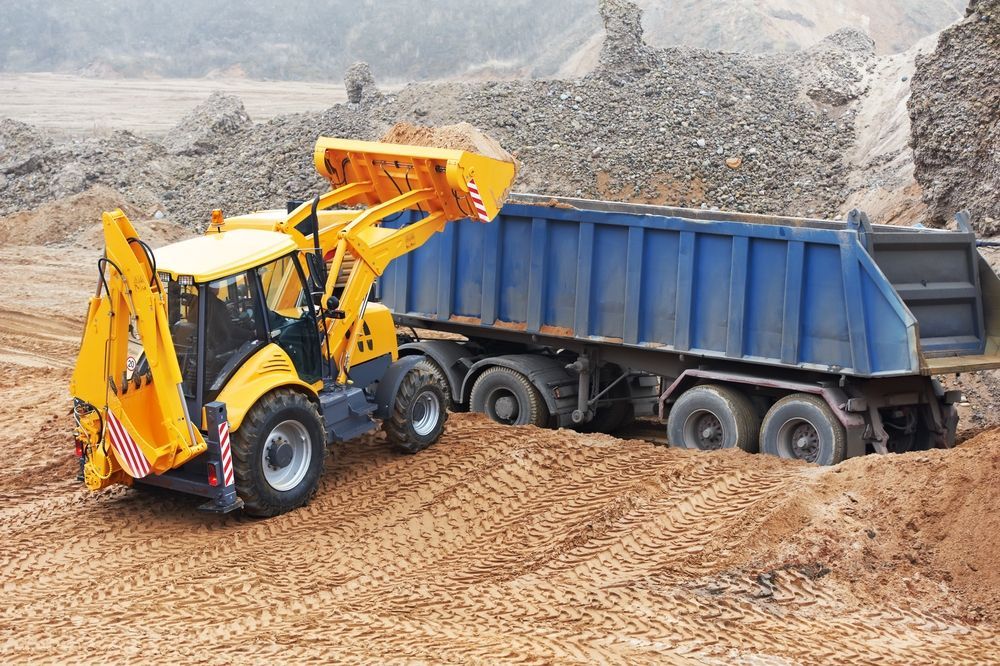 Yellow Loader Dumping Sand Into a Blue Dump Truck at a Construction — Mareeba Crane Hire In Mareeba, QLD