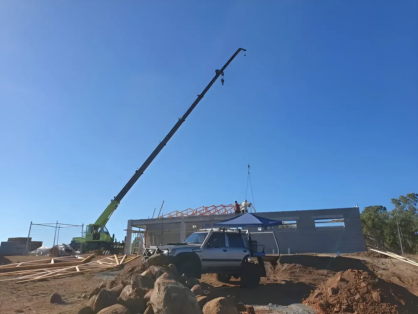 Construction Site with A Crane Lifting Roof Trusses onto A Partially Built Concrete Structure — Mareeba Crane Hire In Mareeba, QLD 