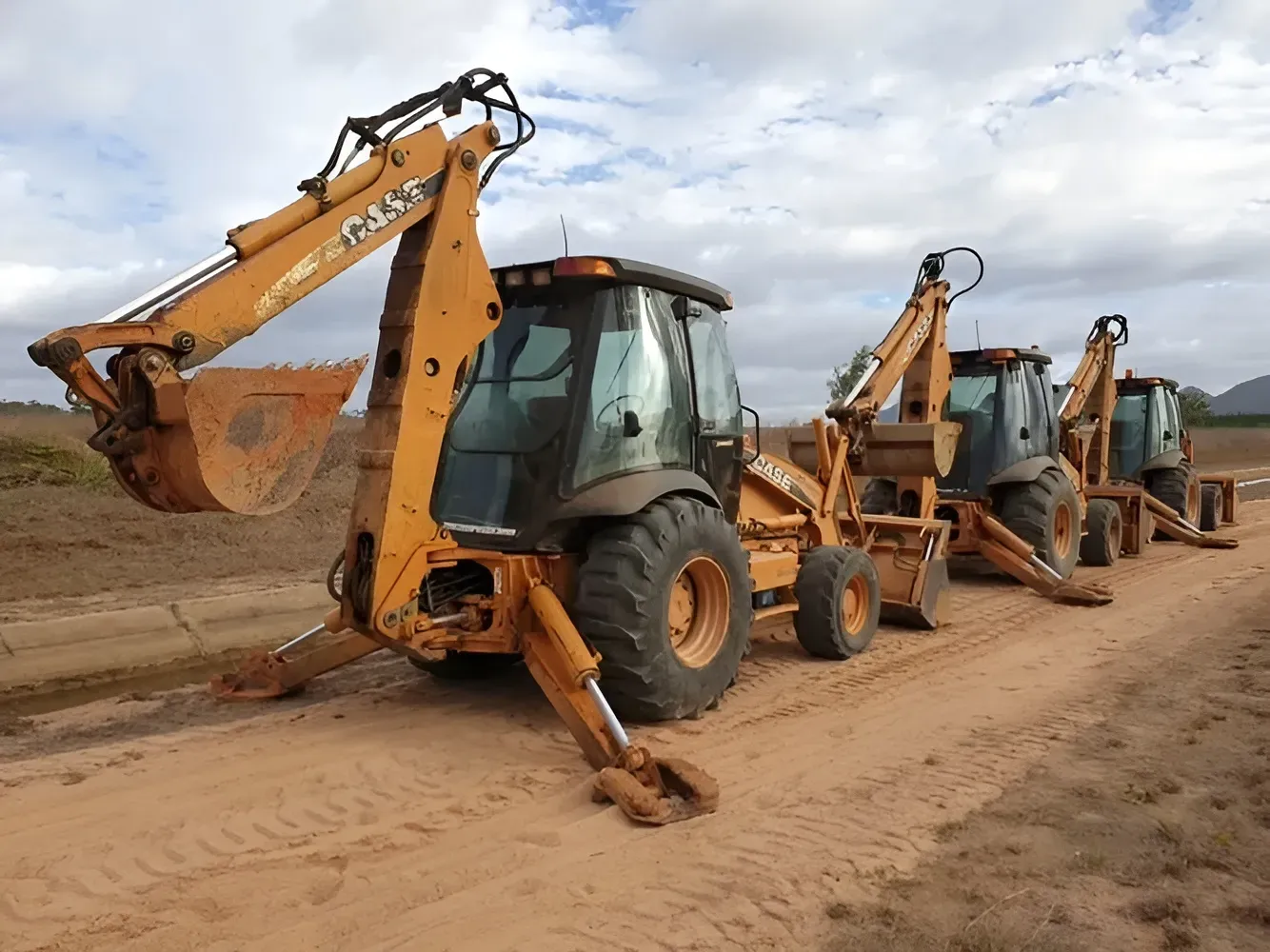 Three Orange Backhoe Loaders Parked on a Dirt Road — Mareeba Crane Hire In Mareeba, QLD