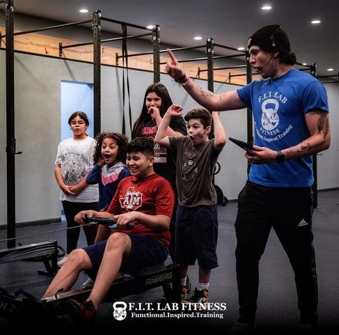 A man in a blue shirt is teaching a group of children how to use a rowing machine.
