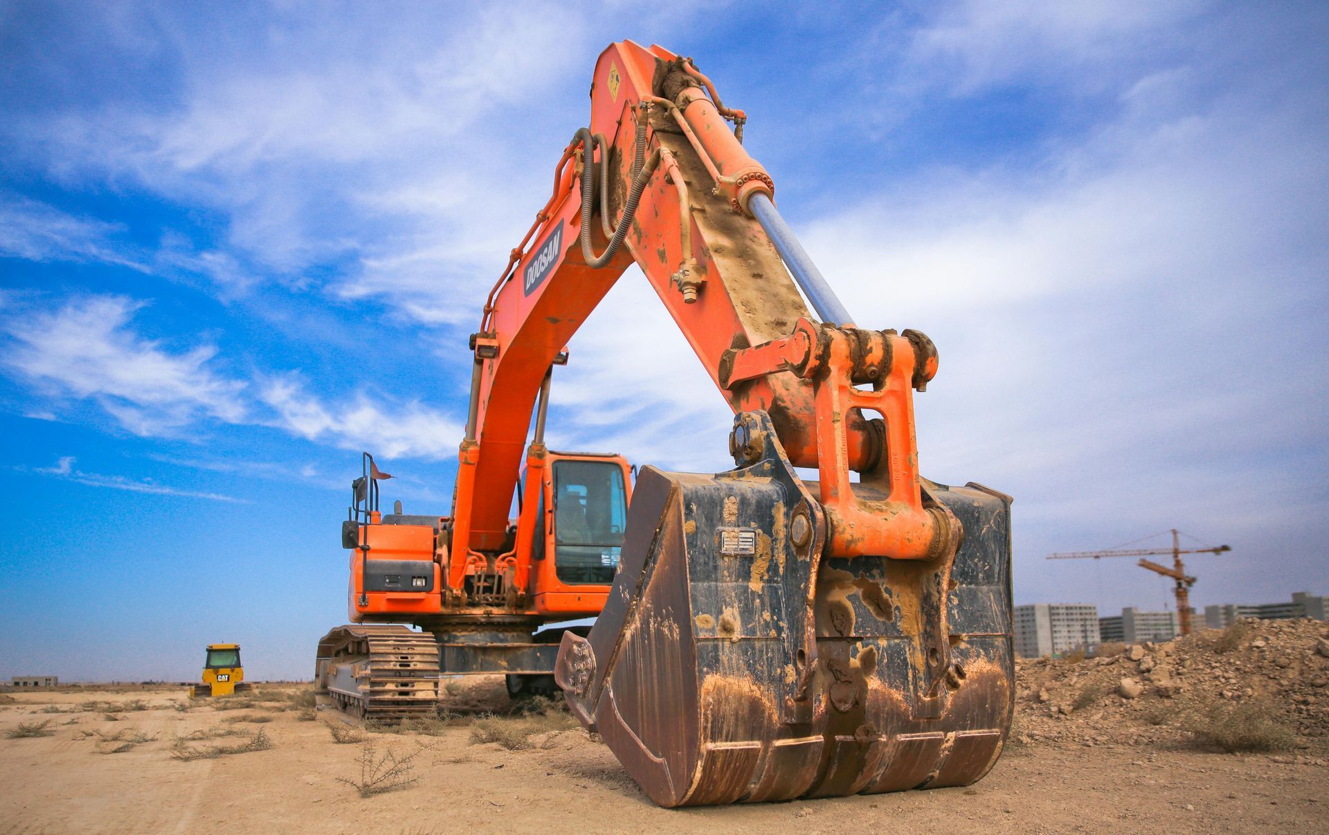 Orange excavator on a construction site, bucket lowered, blue sky background.