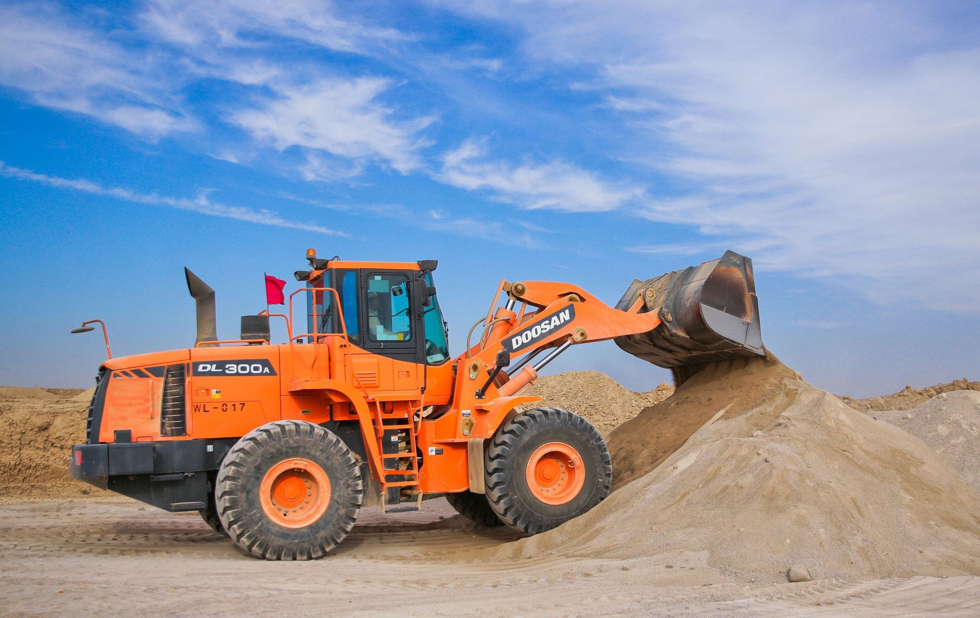 Orange front-end loader dumping sand onto a pile under a blue sky.