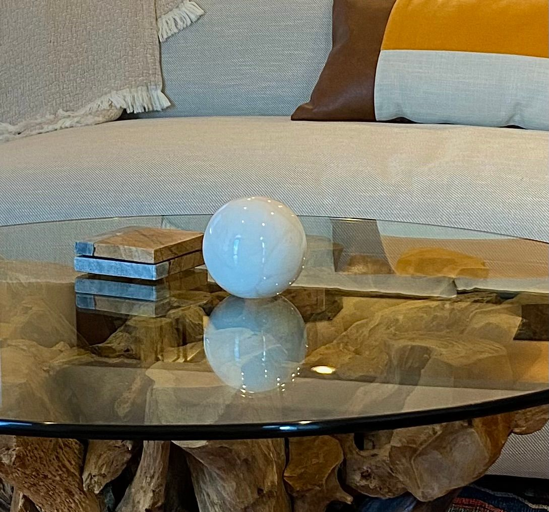 White sphere reflected on a glass-topped table, near a stacked stone block. Couch with pillows in the background. By Robin Bradley Designs 