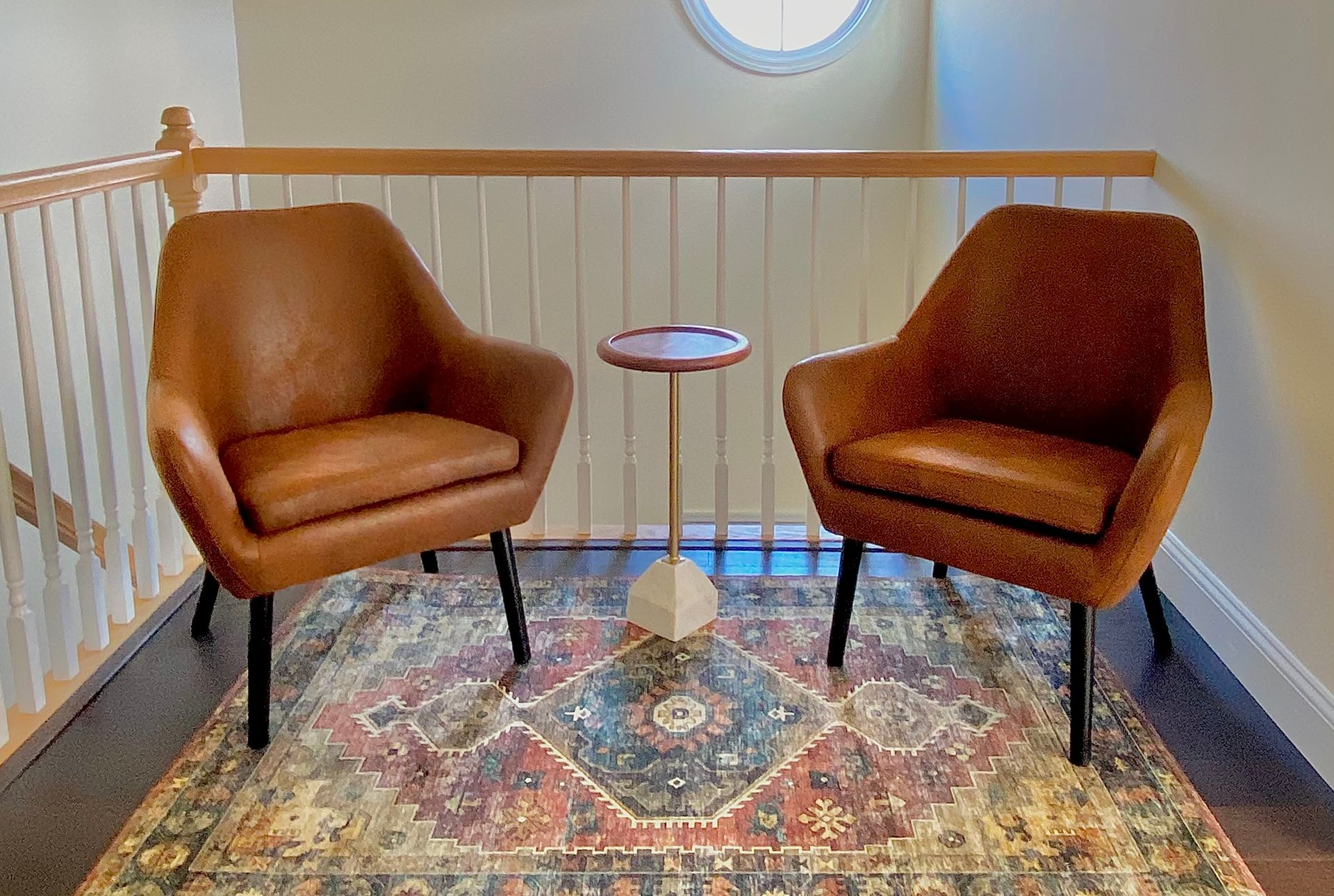 Seating design by Robin Bradley Designs Two brown leather armchairs on a rug with a small table between them; a round window in the background.