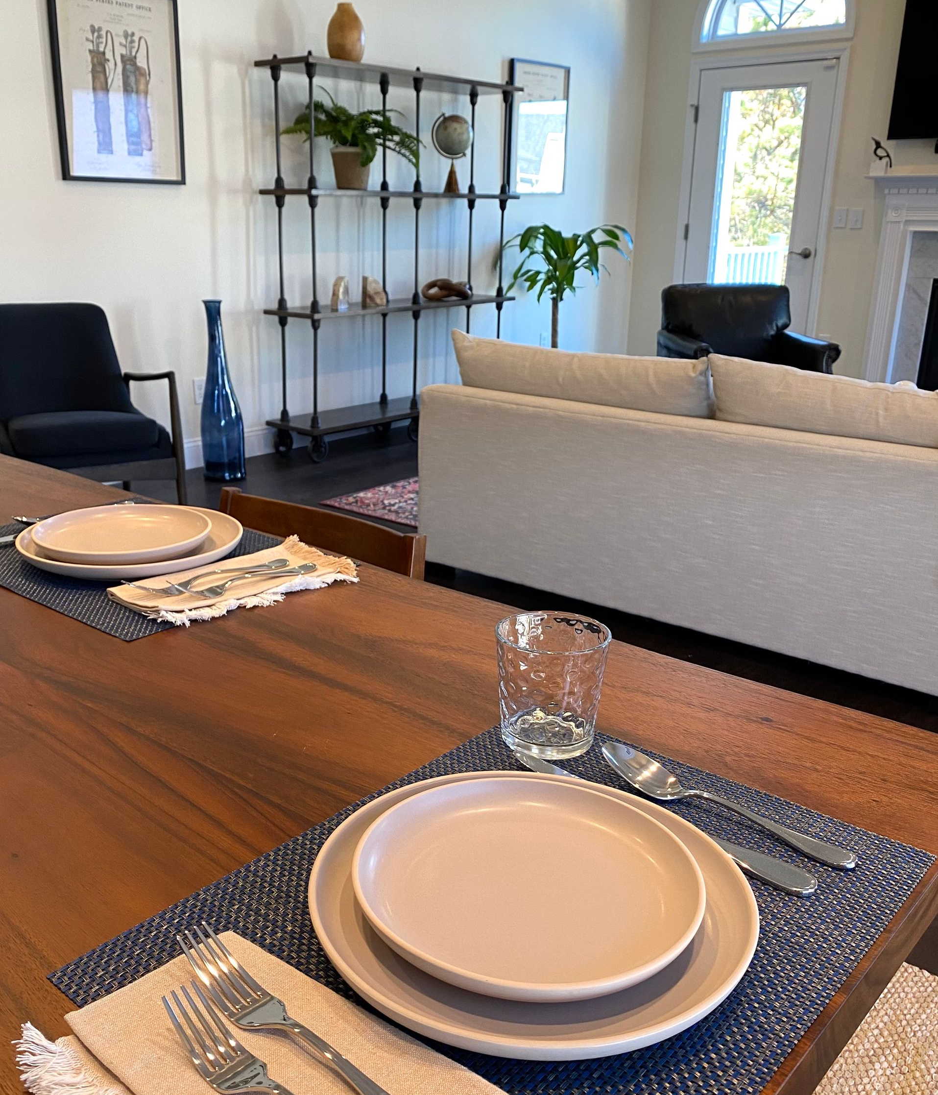 Dining table set for two, with plates, silverware, and a water glass. A living area is visible in the background. Dining Area by Robin Bradley Designs 