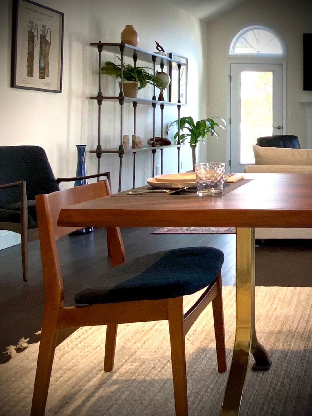 A dining area with a wooden table and chair, shelves with plants, and an arch-topped door. By Robin Bradley Designs