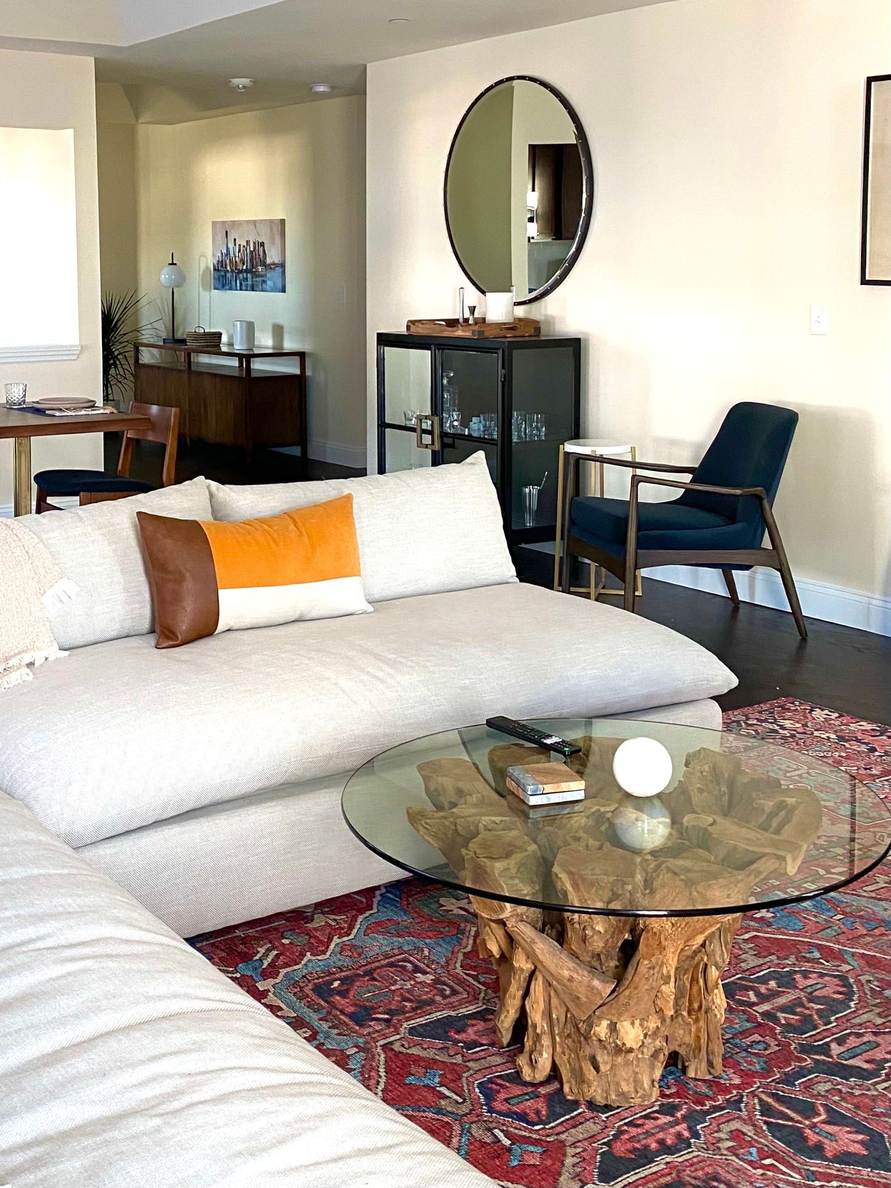 Living room: White sectional, wood table with glass top, red rug, round mirror, dark chair. By Robin Bradley Designs