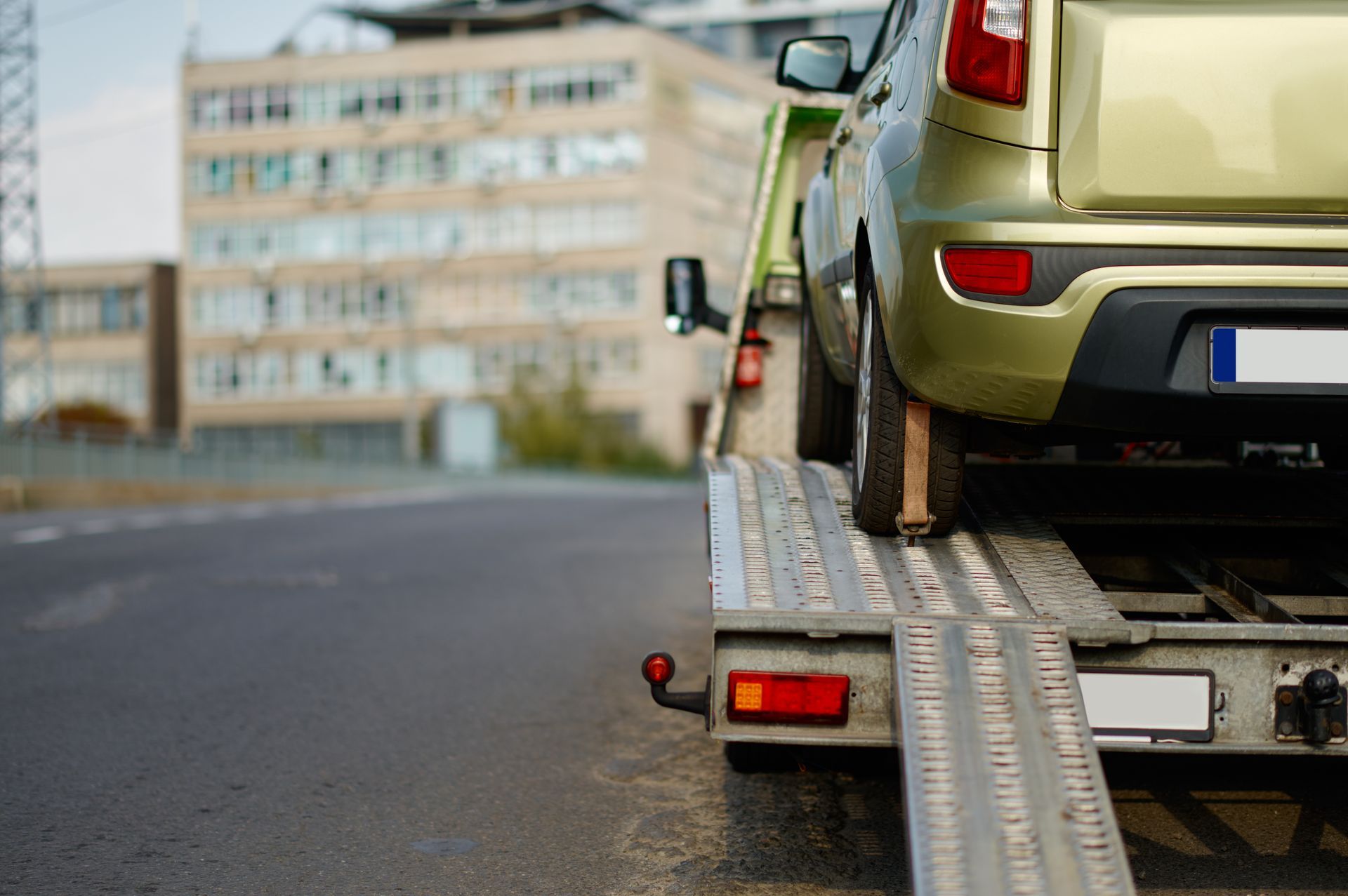 Green car on a tow truck ramp; parked on a road next to a building. Green car on a tow truck ramp; parked on a road next to a building.