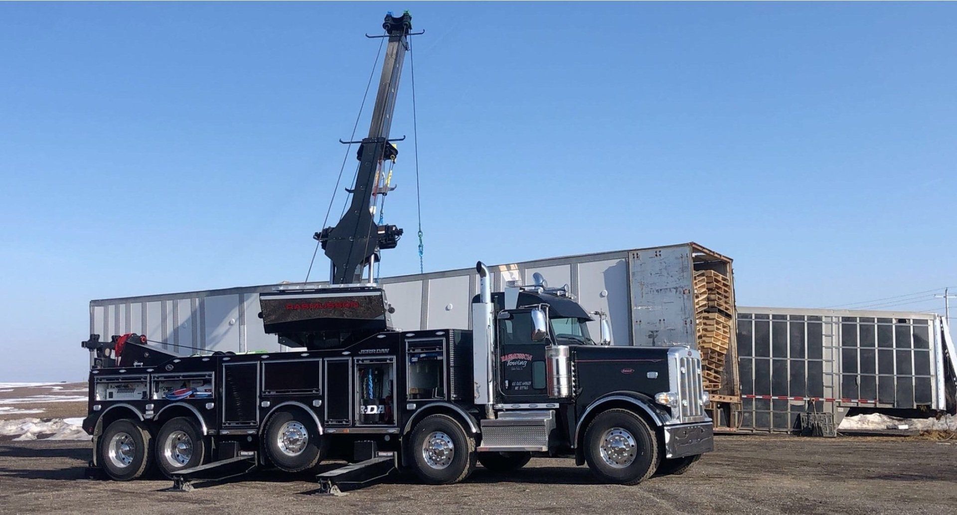 A black truck with a crane attached to it is parked in a dirt field.
