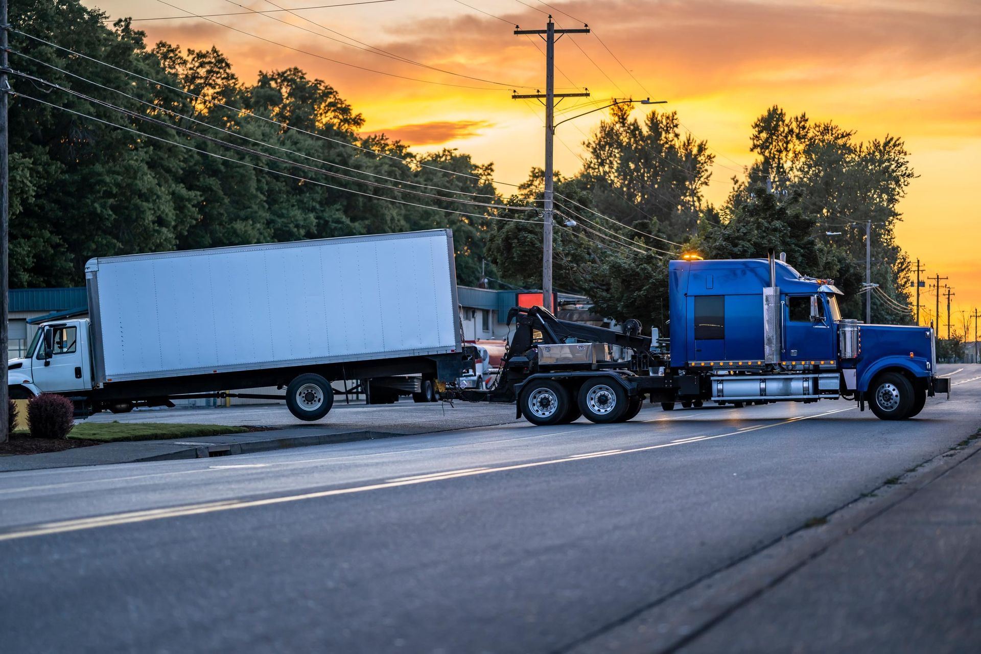 A blue tow truck towing a white truck.
