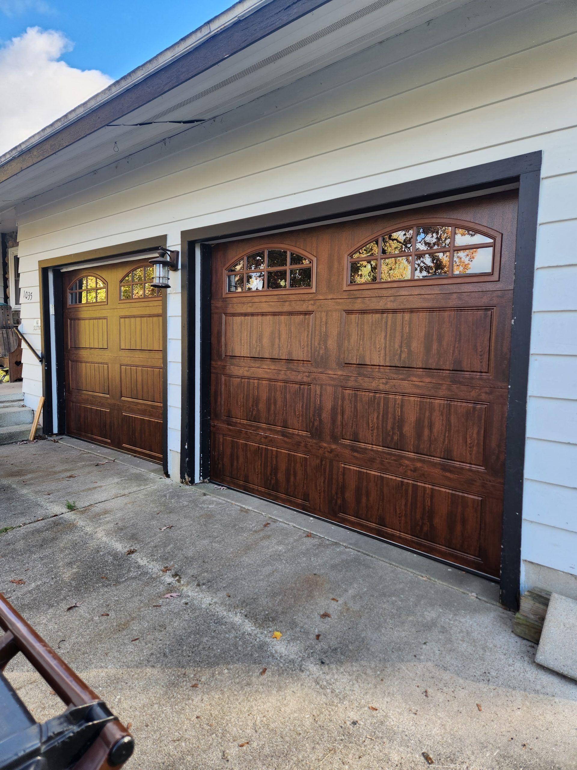 Two brown garage doors on a light-colored house. One door has windows at the top. Gray concrete driveway.
