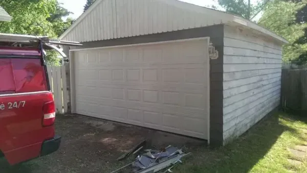 White garage with tan trim, a red truck on the left, and green grass in the background.