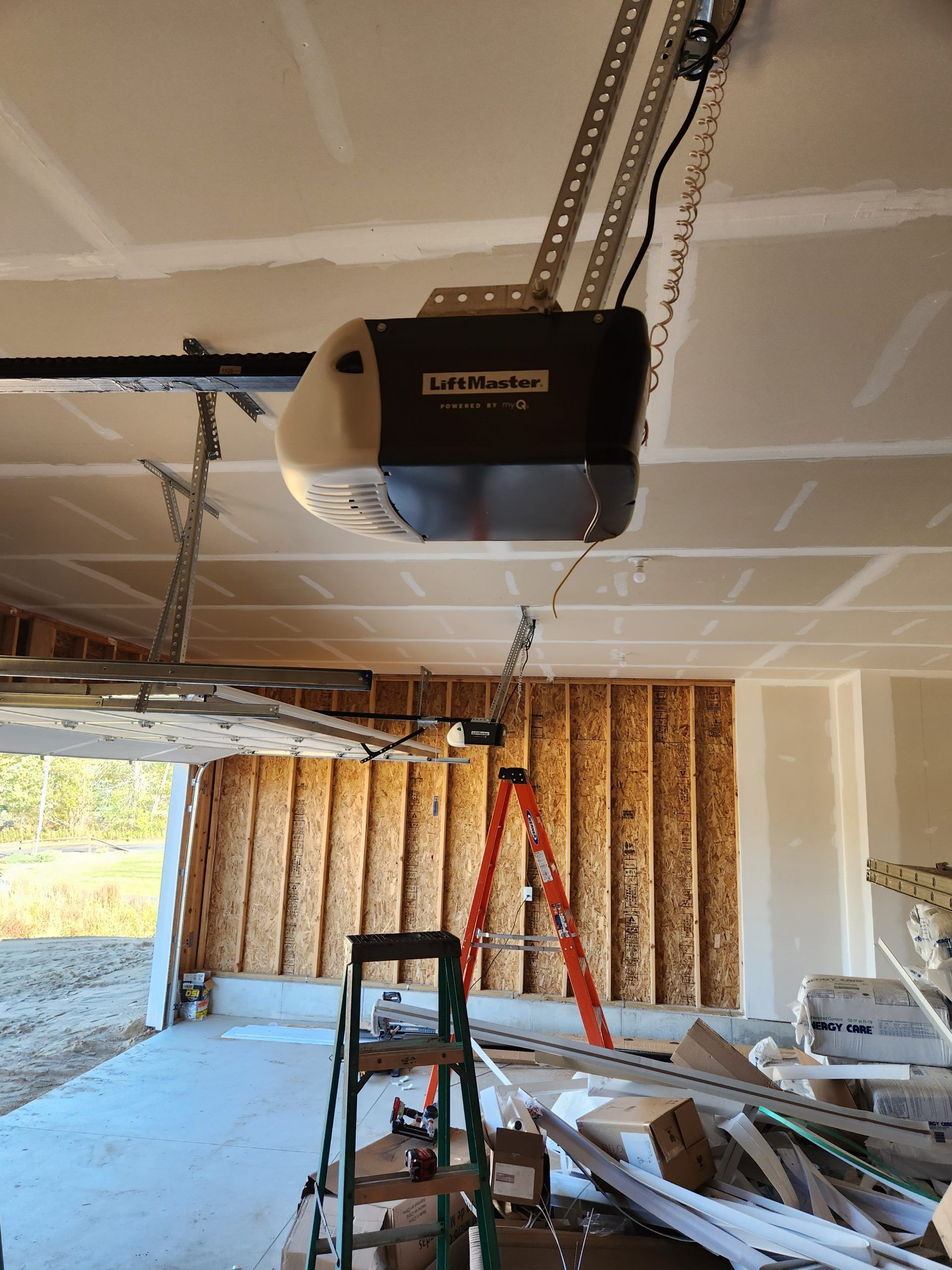 Garage ceiling with a LiftMaster garage door opener installed. Open garage door with ladder in the center.