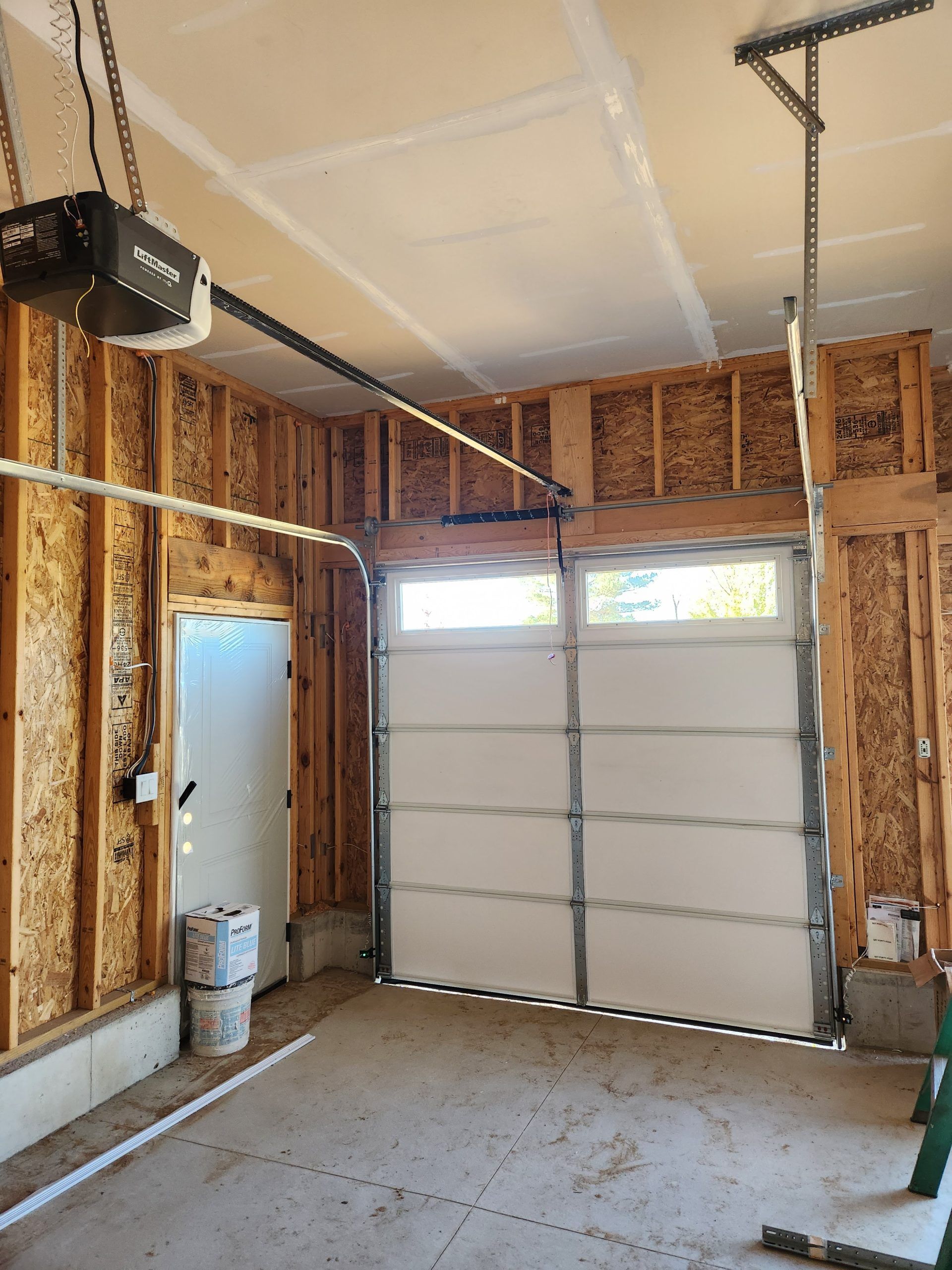 Garage interior with white garage door open, unfinished walls, and an electric opener.