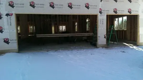 Garage under construction with snow on the ground; wooden frame with windows and open garage door frame.