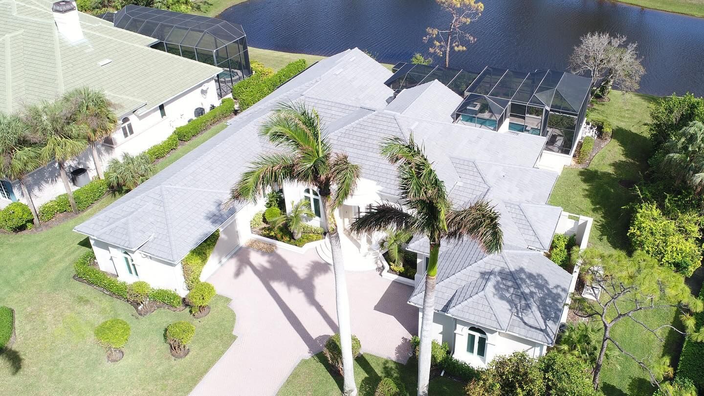 An aerial view of a large house with palm trees and a lake in the background.