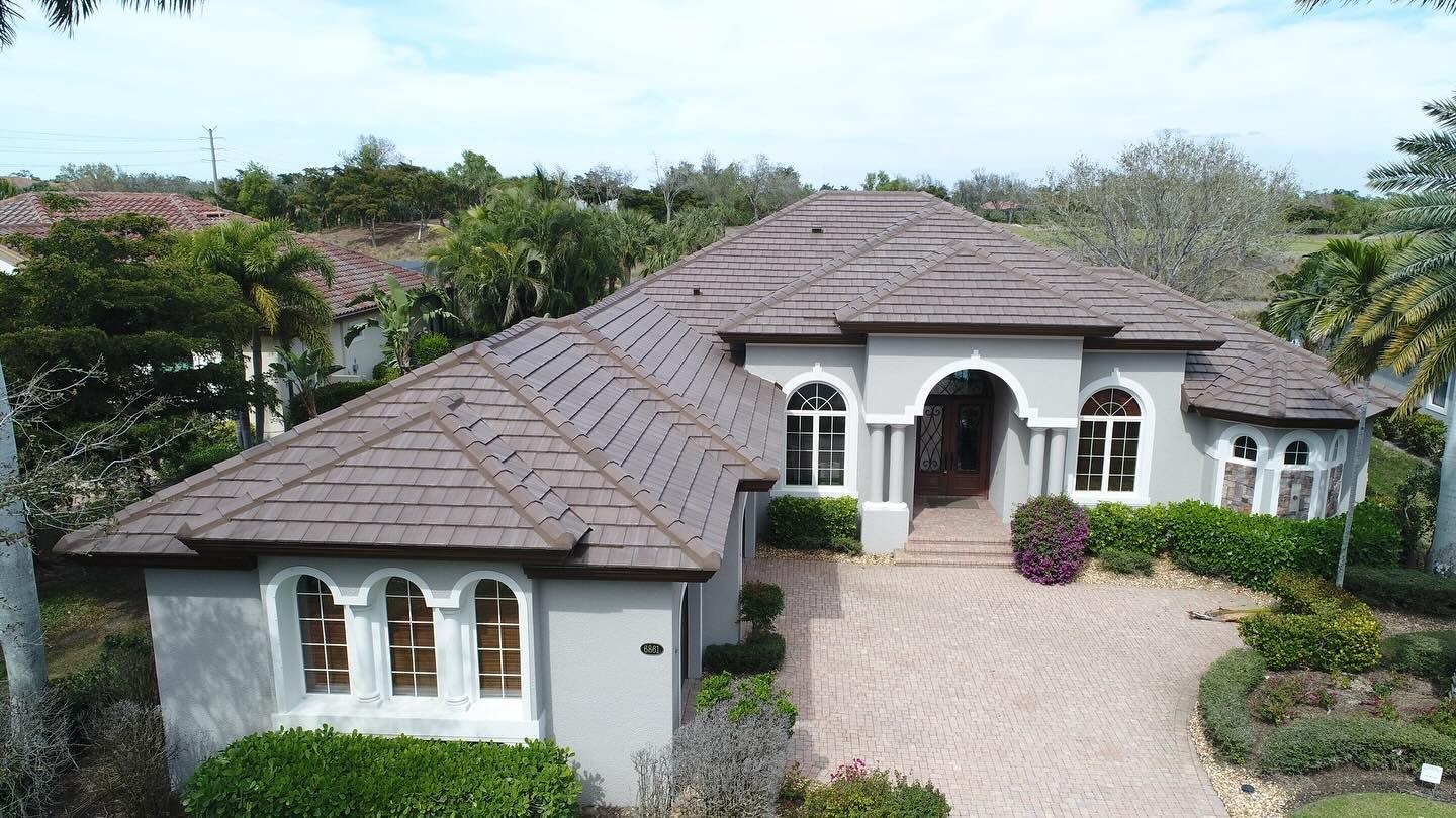 An aerial view of a large white house with a brown roof and a driveway.