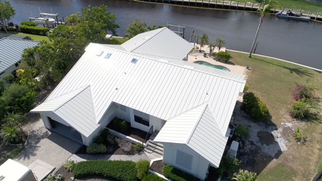 An aerial view of a house with a white roof next to a body of water.