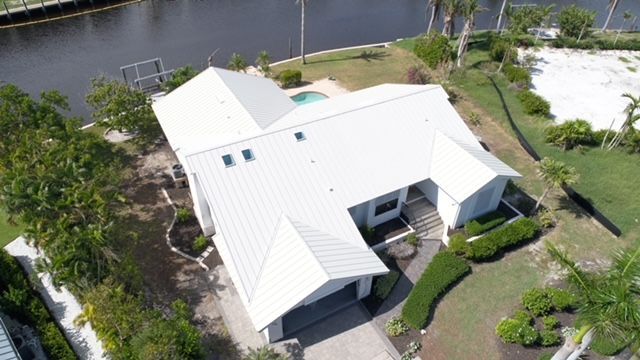 An aerial view of a house with a white roof next to a body of water.