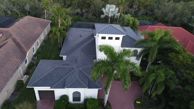 An aerial view of a large white house with a gray roof surrounded by palm trees.