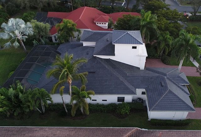 An aerial view of a large house with a gray roof surrounded by palm trees.