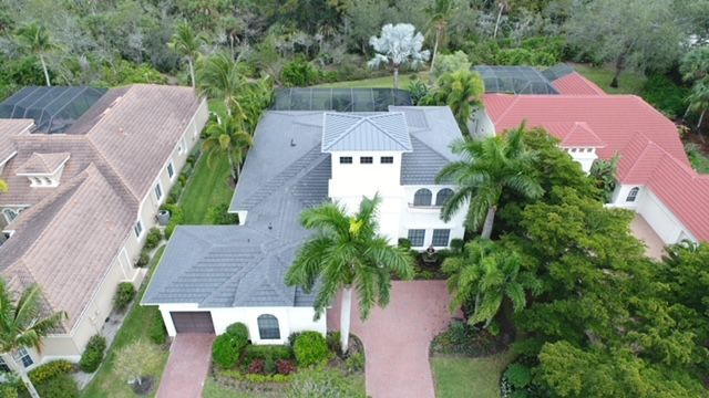 An aerial view of a large white house with a red roof surrounded by palm trees.