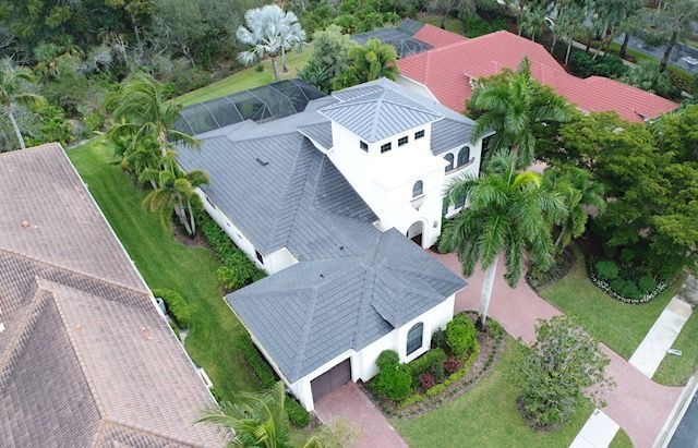 An aerial view of a large white house with a gray roof surrounded by palm trees.