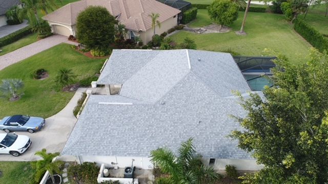 An aerial view of a house with a gray roof and a blue car parked in front of it.