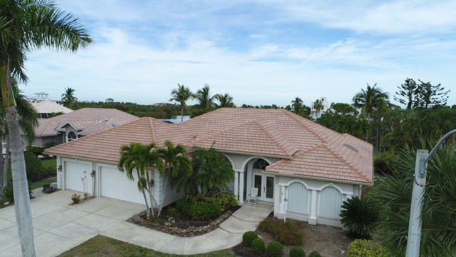 An aerial view of a house with a red tile roof surrounded by palm trees.