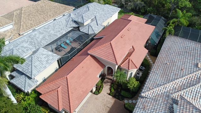 An aerial view of a large house with a red tile roof surrounded by other houses.