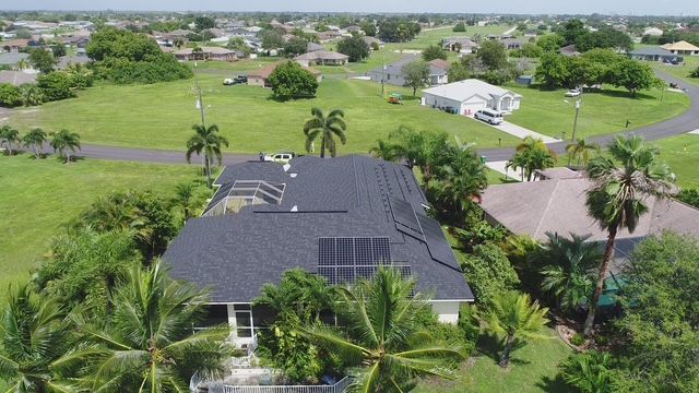An aerial view of a house with solar panels on the roof surrounded by palm trees.