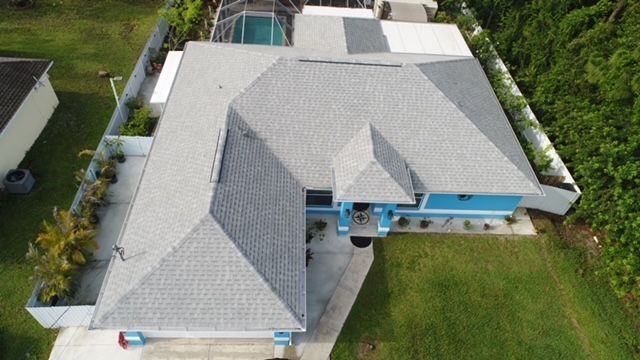 An aerial view of a large house with a gray roof and a pool.