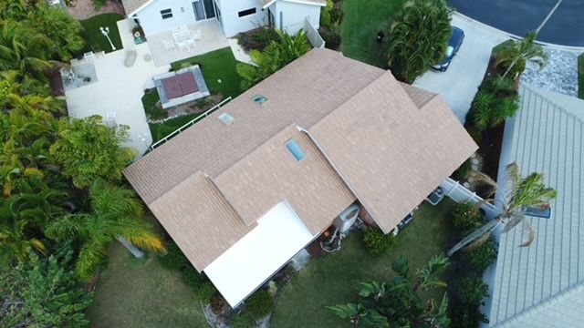 An aerial view of a house with a brown roof surrounded by trees.