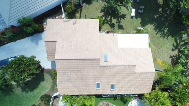 An aerial view of a house with a roof surrounded by trees and grass.