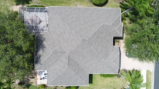 An aerial view of a house with a gray roof surrounded by trees.