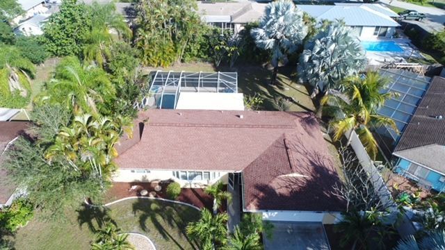 An aerial view of a house with a red roof surrounded by palm trees.