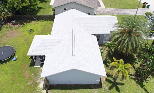 An aerial view of a white house with a trampoline in the backyard.