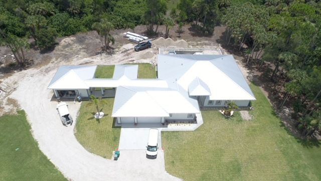 An aerial view of a large house with a white roof surrounded by trees.
