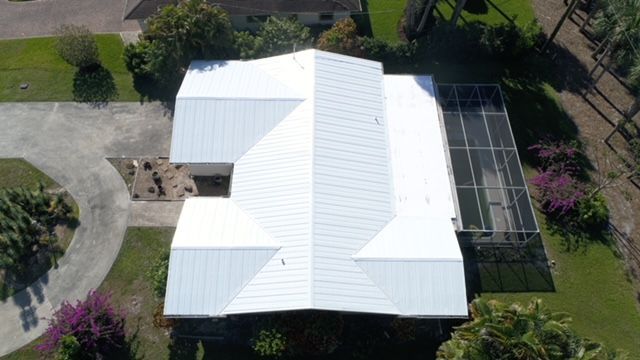 An aerial view of a house with a white roof and a screened in porch.