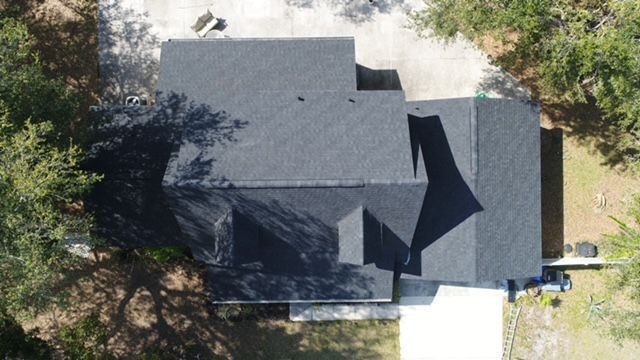 An aerial view of a house with a black roof surrounded by trees.