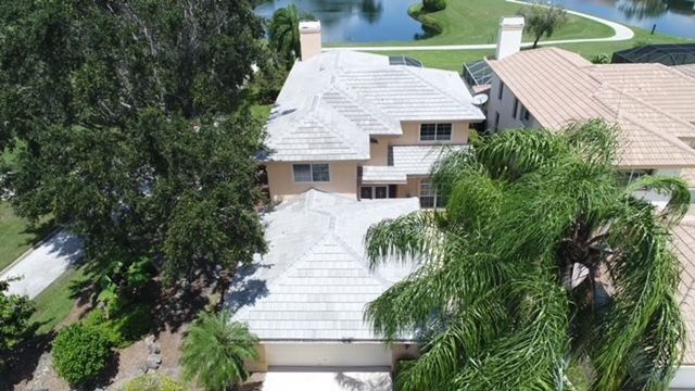 An aerial view of a large house with a white roof surrounded by palm trees.