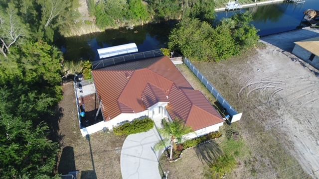 An aerial view of a house with a red roof next to a body of water.