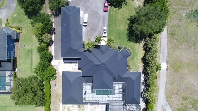 An aerial view of a large house with a black roof surrounded by trees and grass.
