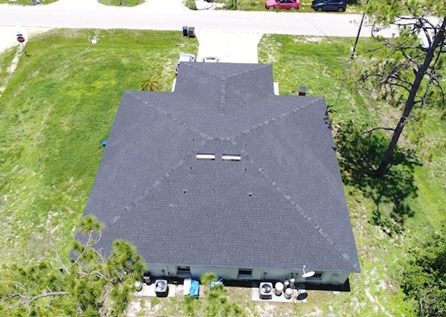 An aerial view of a house with a black roof surrounded by grass and trees.
