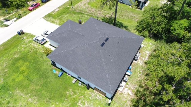 An aerial view of a house with a black roof surrounded by trees and grass.