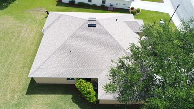 An aerial view of a house with a roof and a tree in front of it.