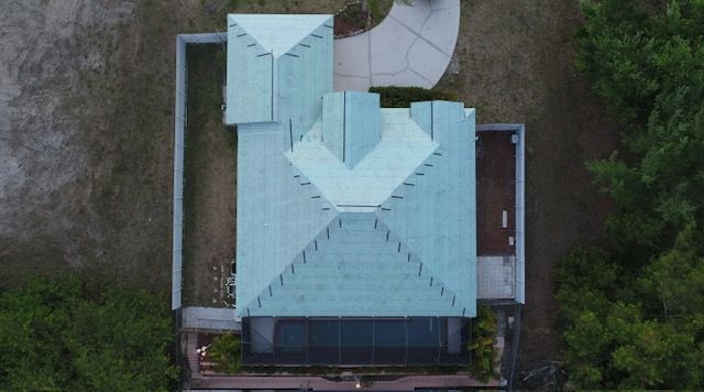 An aerial view of a house with a green roof surrounded by trees.