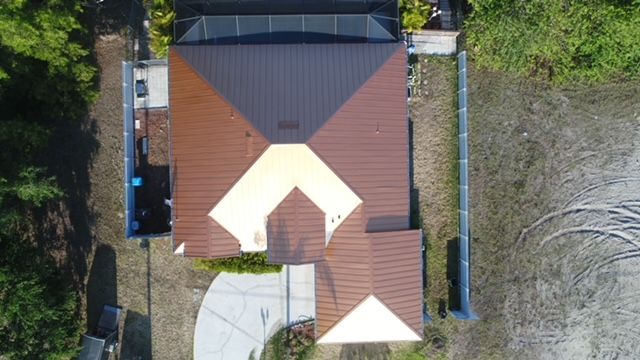 An aerial view of a house with a brown roof surrounded by trees.