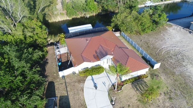 An aerial view of a house with a red roof surrounded by trees and a river.